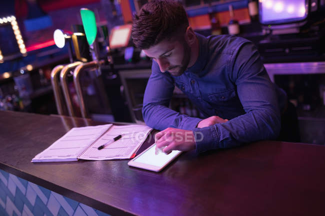 Bartender using digital tablet at counter in bar — Stock Photo