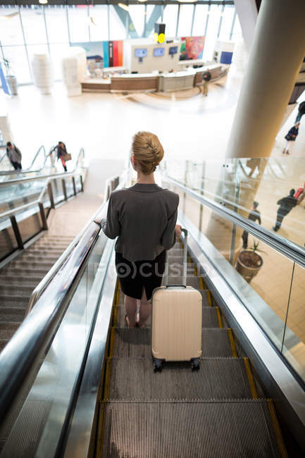 Rear view of businesswoman standing on escalator with luggage at airport — Stock Photo