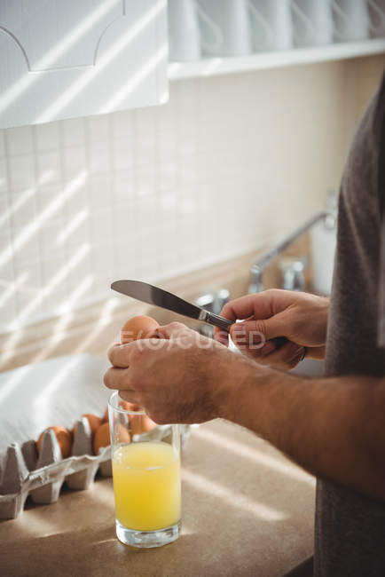 Milieu de section de l'homme craquant oeuf dans un verre dans la cuisine à la maison — Photo de stock