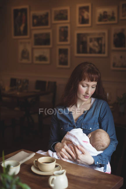 Loving mother holding cute baby in arms at cafe — Stock Photo