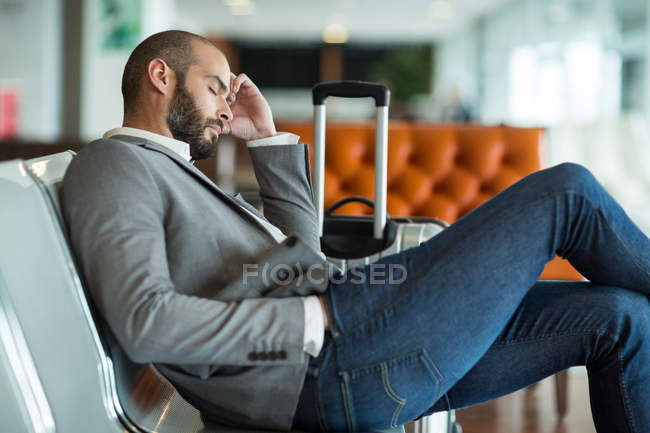 Empresario durmiendo en silla en la sala de espera en la terminal del aeropuerto - foto de stock