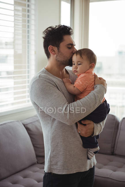 Padre besando a su bebé en la sala de estar en casa - foto de stock