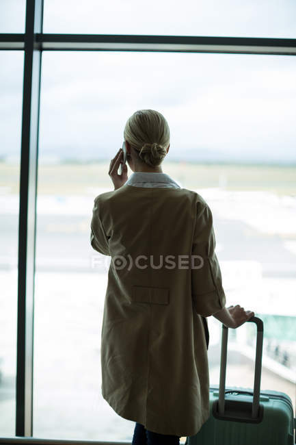 Вид ззаду бізнес-леді з багажем, що розмовляє по мобільному телефону в аеропорту — стокове фото