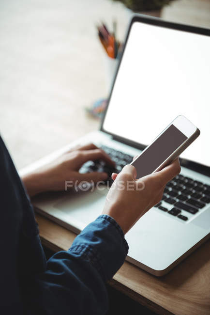 Business executive using mobile phone and laptop in office — Stock Photo