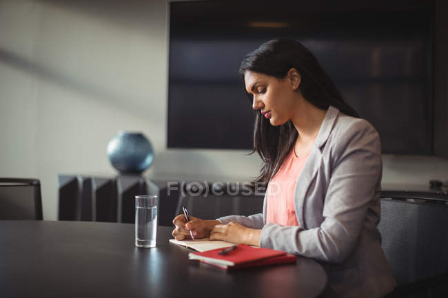 Бізнес-леді, що пише в щоденнику в офісі — стокове фото