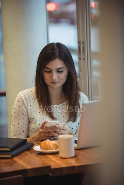 Empresaria que usa teléfono móvil con computadora portátil en la mesa - foto de stock