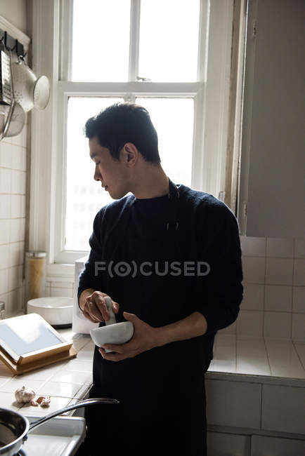 Man using pestle and mortar looking at digital tablet in home — Stock Photo