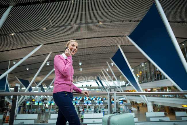 Female commuter with luggage talking on mobile phone in airport — Stock Photo