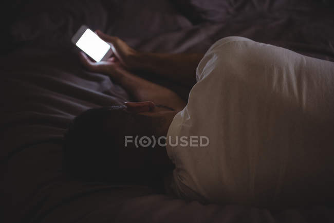 Homme utilisant son téléphone portable tout en se relaxant sur le lit à la maison — Photo de stock