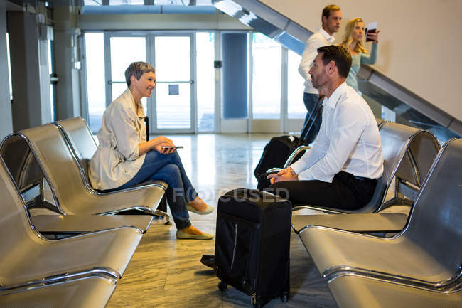 Passageiros com mala interagindo na área de espera no terminal do aeroporto — Fotografia de Stock