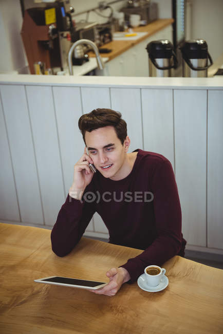 Man talking on mobile phone and holding digital tablet in coffee shop — Stock Photo