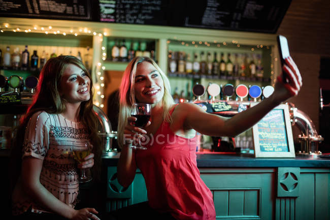 Amigos tirando selfie do celular enquanto bebem vinho no balcão no bar — Fotografia de Stock