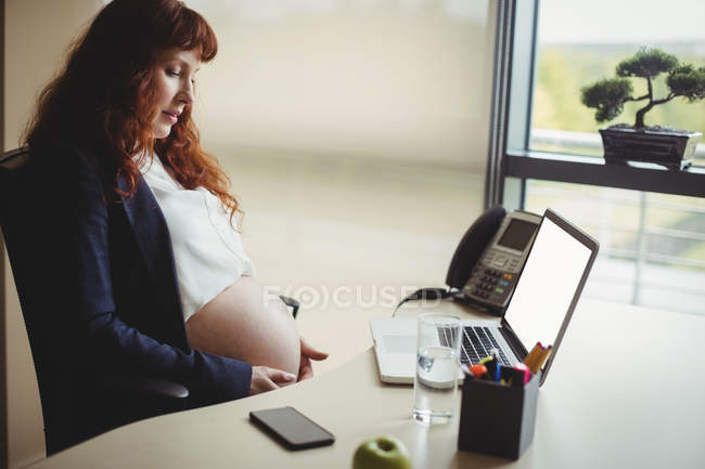 Donna d'affari incinta che tocca la pancia in ufficio — Foto stock
