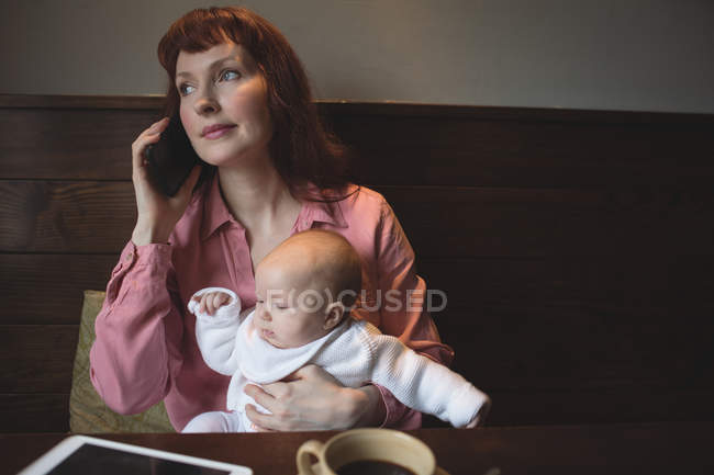 Mère avec bébé parlant sur un téléphone portable dans un café — Photo de stock