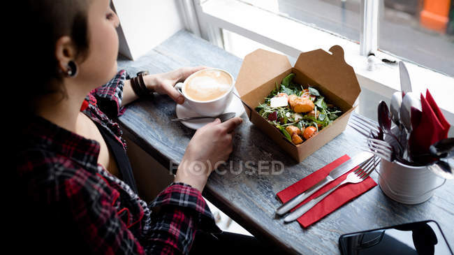 Belle femme prenant du café et de la salade dans le café — Photo de stock