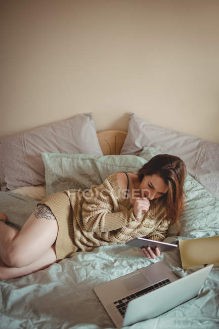 Schöne Frau mit digitalem Tablet und Laptop auf dem Bett zu Hause — Stockfoto