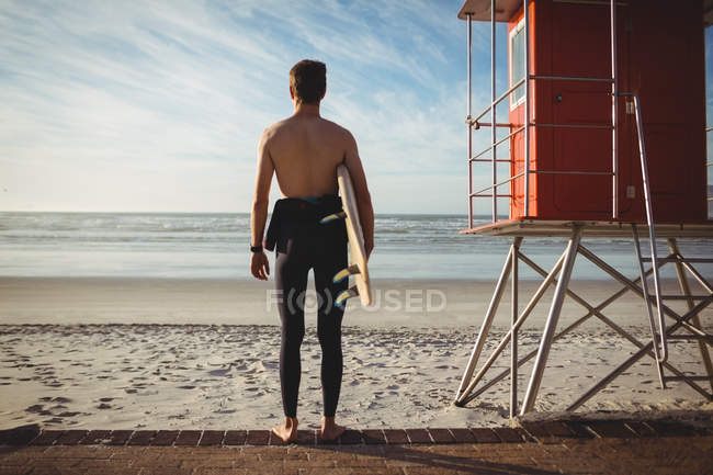 Vue arrière du surfeur debout avec planche de surf sur la plage — Photo de stock