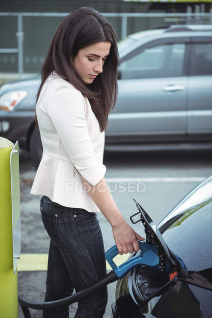 Красива жінка заряджає електромобіль на вулиці — стокове фото