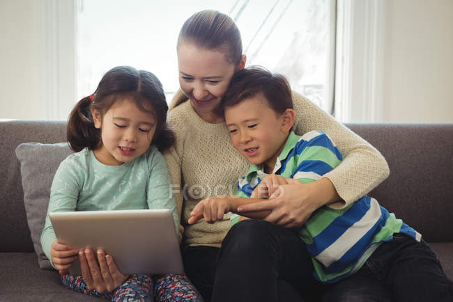 Smiling mother and kids using digital tablet in living room — Stock Photo