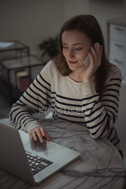 Жінка розмовляє по телефону, використовуючи ноутбук вдома — стокове фото