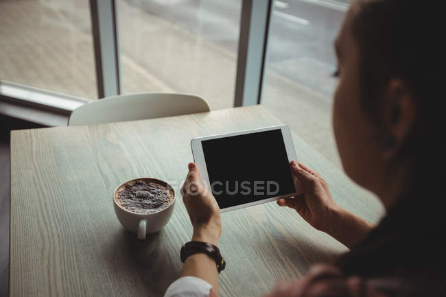 Mujer usando tableta digital mientras toma una taza de café en la cafetería - foto de stock