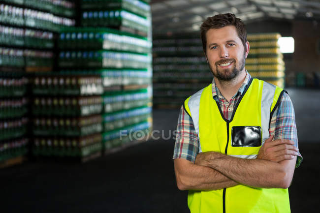 Retrato de un trabajador varón confiado con los brazos cruzados de pie en el almacén - foto de stock