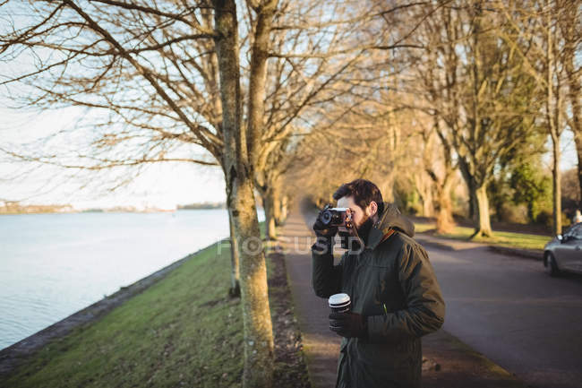 Мужчина фотографируется с камерой возле реки в парке — стоковое фото