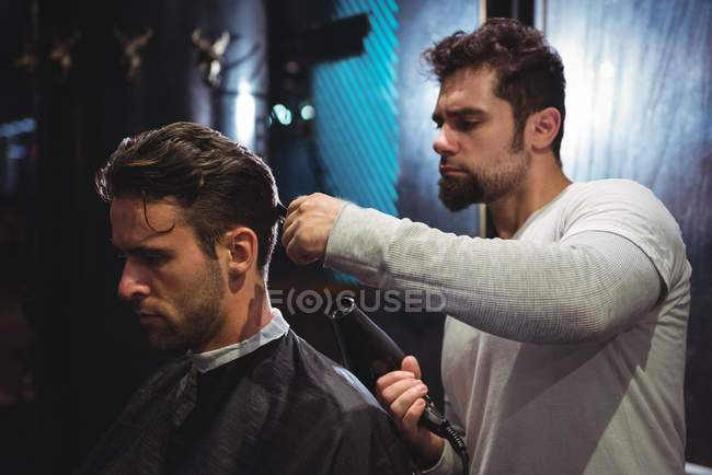 Barber blow drying client hair in barber shop — Stock Photo