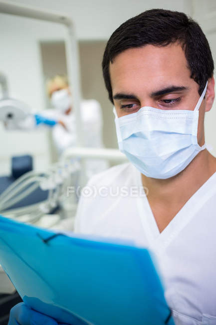 Dentista in maschera chirurgica guardando una cartella clinica dentistica — Foto stock