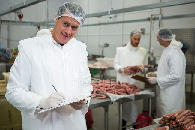 Portrait of male butcher maintaining records on clipboard at meat factory — Stock Photo