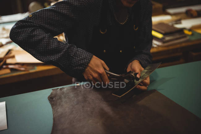 Mid-section of craftswoman punching hole from leather punch machine in workshop — Stock Photo