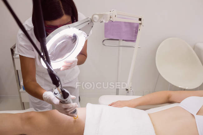 Close-up de médico realizando depilação a laser na pele da coxa do paciente na clínica — Fotografia de Stock