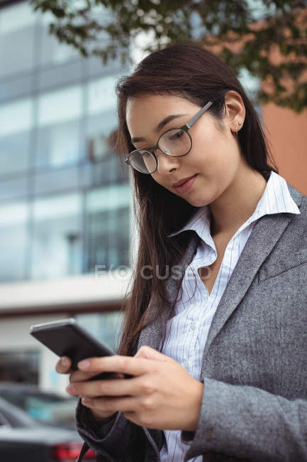 Бізнес-леді текстові повідомлення на мобільному телефоні, стоячи на міській вулиці — стокове фото