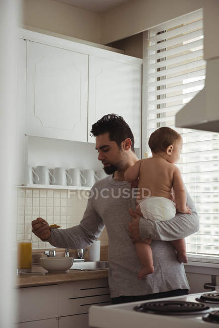 Отец завтракает, держа ребенка на кухне — стоковое фото