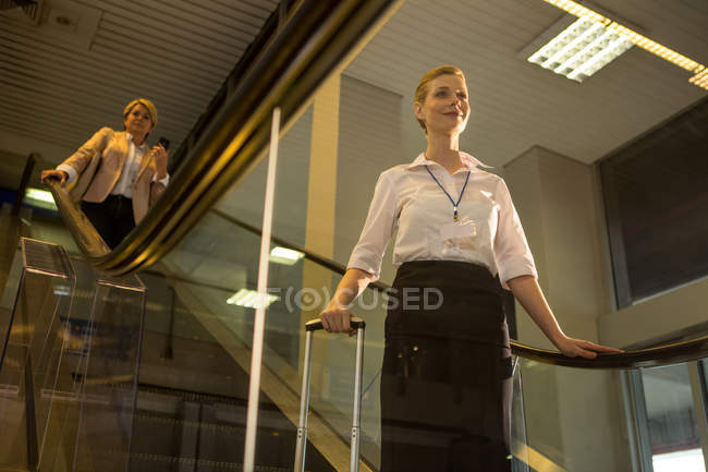Female staff coming down from the escalator in the airport terminal — Stock Photo