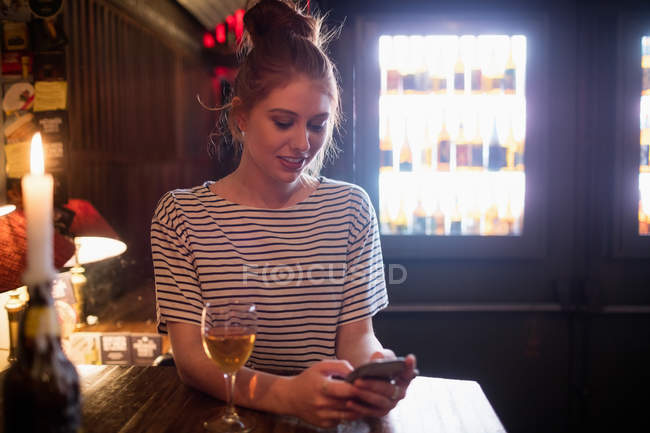 Женщина, использующая мобильный телефон с вином на столе в баре — стоковое фото