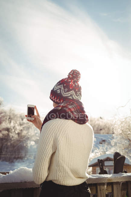 Вид ззаду жінки, що фотографується за допомогою мобільного телефону на гірськолижному курорті — стокове фото