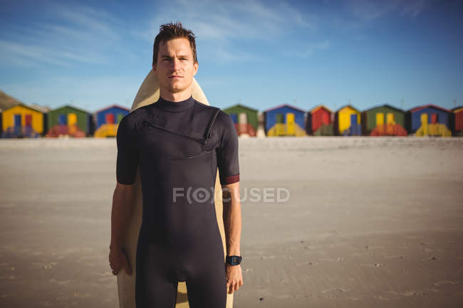 Vista frontal del surfista de pie con tabla de surf en la playa - foto de stock