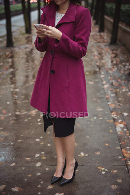 Обрезанный вид предпринимательницы с помощью телефона, стоящего на осеннем пути — стоковое фото
