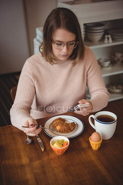 Жінка використовує мобільний телефон під час сніданку у вітальні вдома — стокове фото