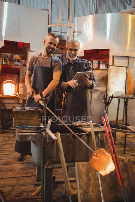 Team of glassblowers using digital while working over a molten glass at glassblowing factory — Stock Photo