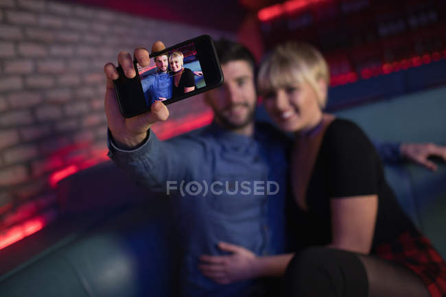 Smiling couple taking selfie on mobile phone in bar — Stock Photo