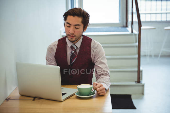 Homem usando laptop enquanto toma café na cafeteria — Fotografia de Stock