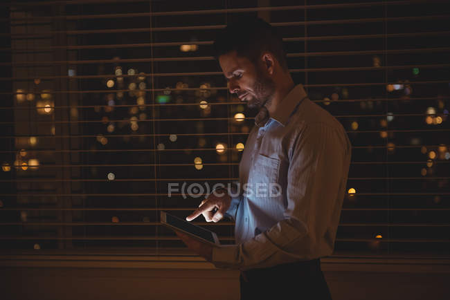 Homem usando seu tablet digital perto de persianas à noite — Fotografia de Stock