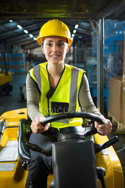 Ritratto di bella lavoratrice che guida carrello elevatore in magazzino — Foto stock