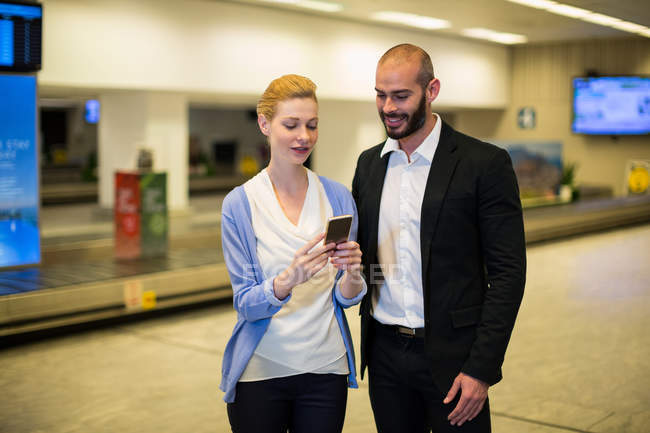 Усміхнене пара, дивлячись на мобільний телефон у зону очікування в аеропорту терміналу — стокове фото