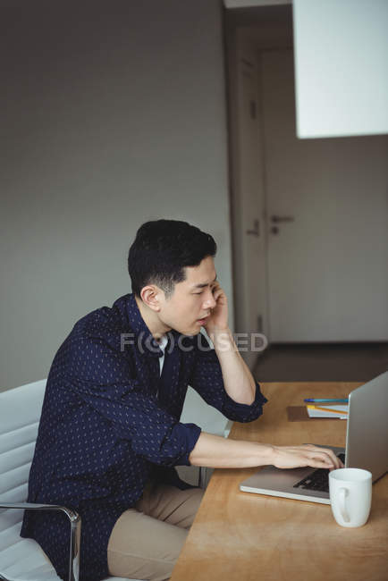 Executivo de negócios falando no telefone celular enquanto usa laptop no escritório — Fotografia de Stock