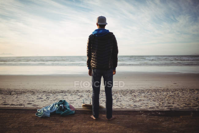 Вид сзади на босоногого человека с доской для серфинга, стоящей на пляже — стоковое фото