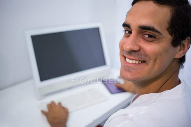 Retrato de médico sonriente usando PC de escritorio en la clínica - foto de stock
