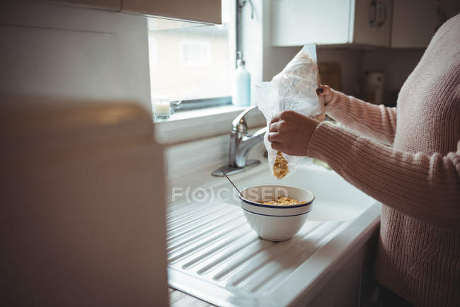 Femme versant des céréales dans un bol à la cuisine — Photo de stock